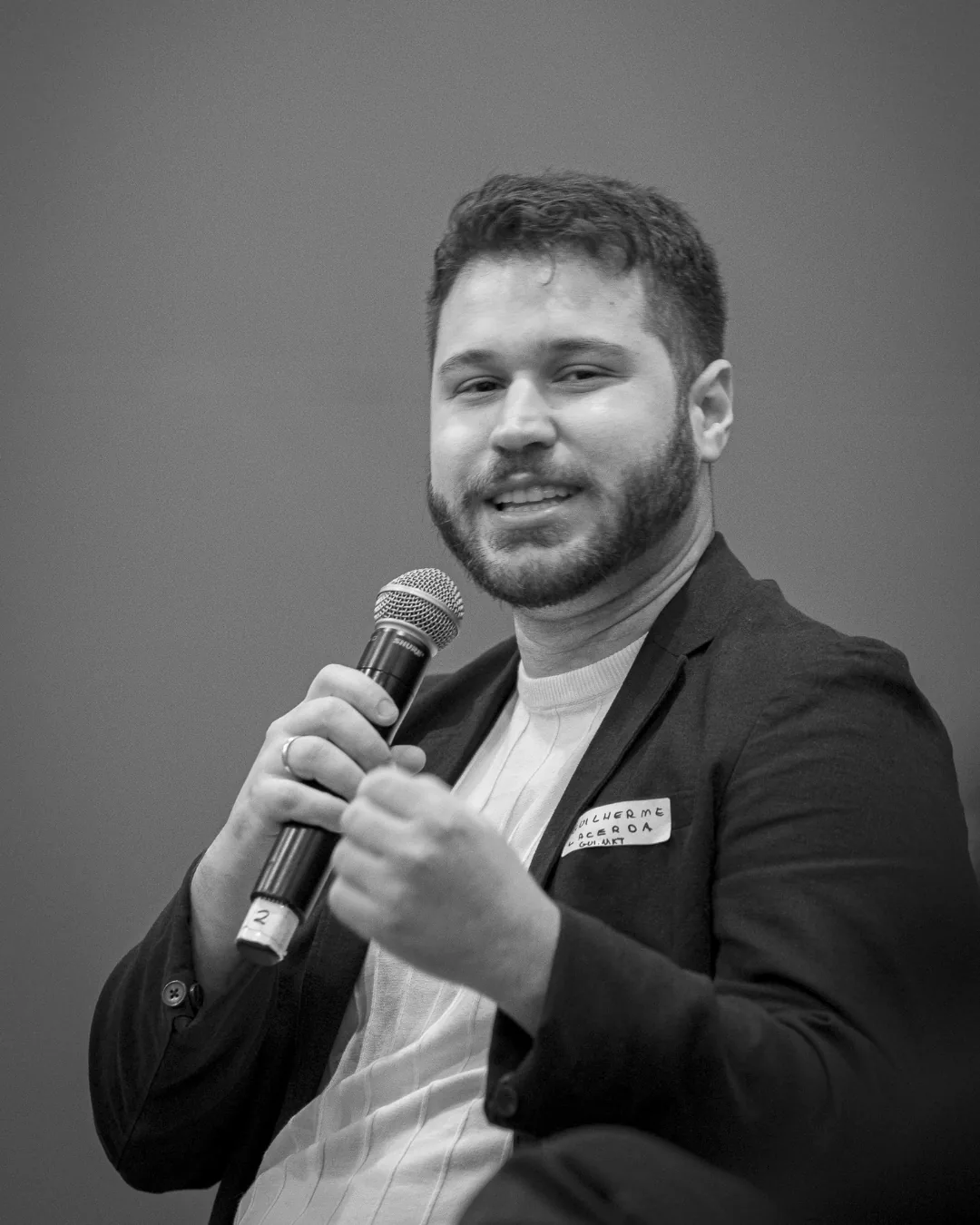 Guilherme Lacerda falando ao microfone, em fotografia em preto e branco.