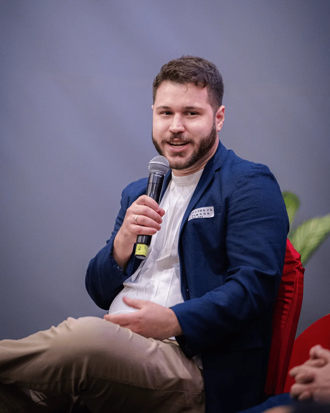 Guilherme Lacerda sentado, conversando ao microfone durante um evento.