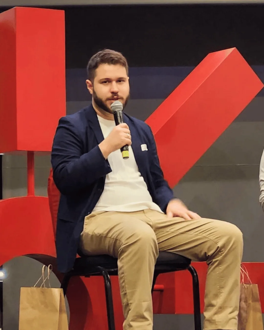 Guilherme Lacerda participando de uma conversa em palco com cenário vermelho.